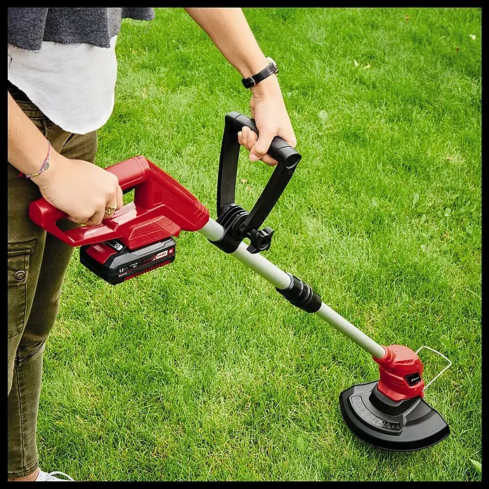 Einhell Power X-Change 18V Akku-Rasentrimmer - 18 V, 2 Ah, Li-Ionen, 1 Akku, Schnittbreite Messer: 24 cm - Eine Person hält einen roten Rasentrimmer der Marke Einhell auf einer grünen Rasenfläche.