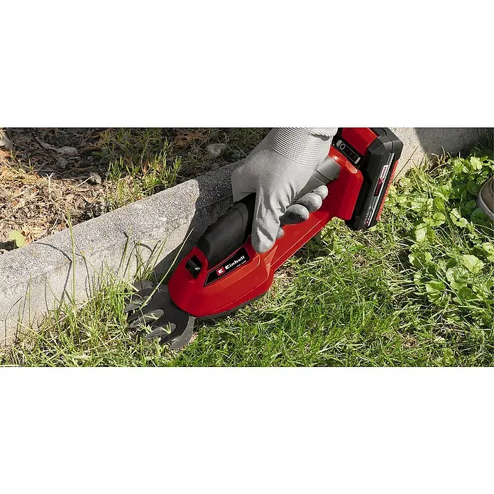 Einhell Power X-Change 18V Akku-Grasschere GE-CG 18/1 LI-SOLO - 18 V, Ohne Akku, Schnittbreite: 100 mm - Nahaufnahme der Akku-Grasschere von Einhell im Einsatz, die von einer behandschuhten Hand gehalten wird, um Gras an einer Bordsteinkante zu trimmen.