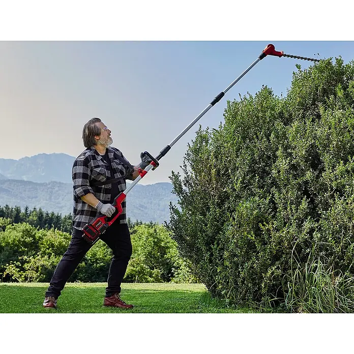 Einhell PXC 18V Multiherramienta de jardín 36VGE-LM 36/4in1 + Batería y cargador PXC-Starter kit - 36 V, Iones de litio, 4 Ah, 2 baterías - Un hombre usa un cortasetos de pértiga inalámbrico Einhell para recortar un seto en un jardín.