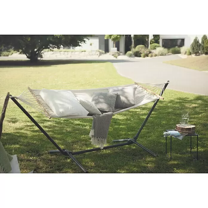 Hängematten-Set mit Gestell - L x B x H: 300 x 105 x 120 cm, Beige - Weiße Hängematte mit gemusterten Kissen und einer grauen Decke auf einem schwarzen Ständer, für Entspannung im Freien aufgestellt.