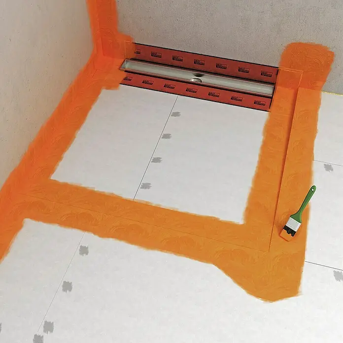 Fermacell Flüssigfolie - 5 kg - Das Bild zeigt eine Duschrinne mit orangefarbener Abdichtung und einem Pinsel, was die Installation oder Wartung der Duschrinne andeutet.