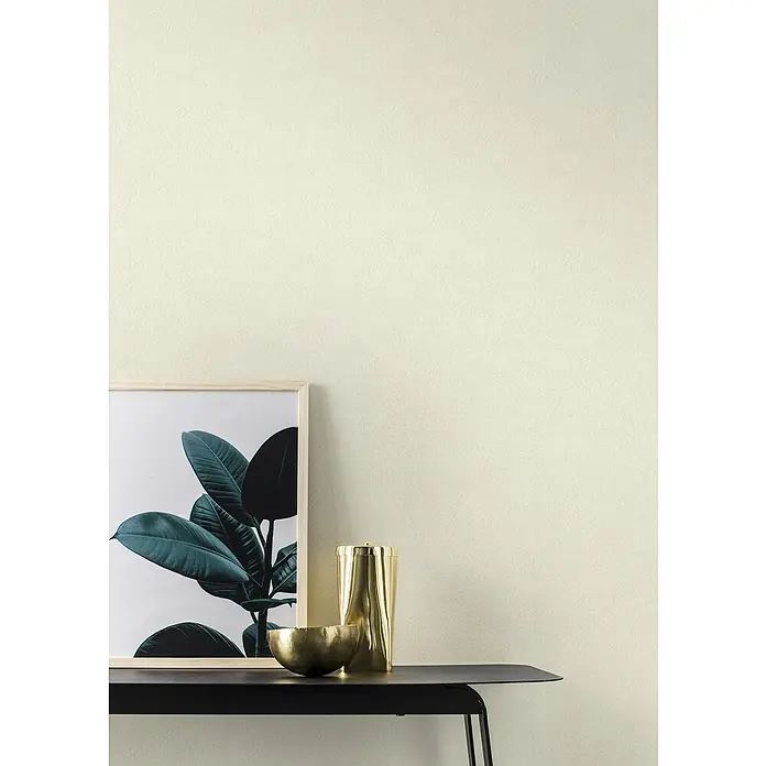 Rasch Saphira Vliestapete I - Weiß, Uni, 10,05 x 0,53 m - Minimalistisches Interieur mit einer gerahmten Pflanze, einer goldenen Schale und einem goldenen Behälter auf einem schwarzen Tisch vor einer strukturierten Wand.