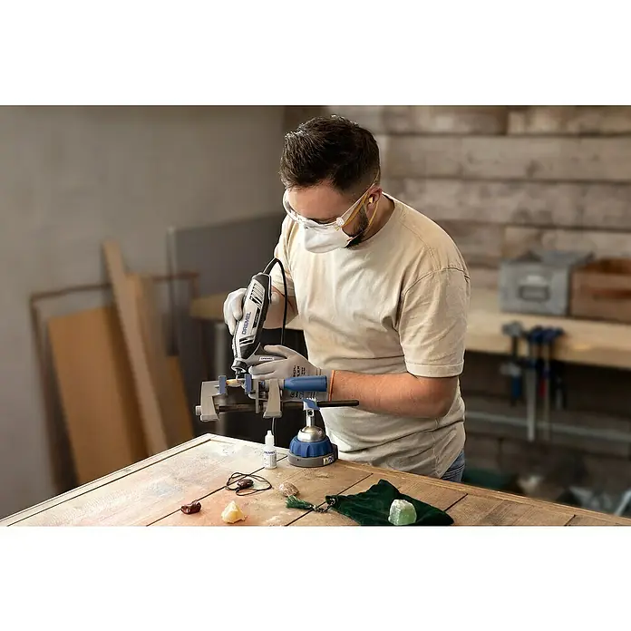 Dremel Multifunktionswerkzeug 4250-35 - 175 W, 5.000 U/min - 35.000 U/min - Ein Mann benutzt ein Dremel-Rotationswerkzeug mit einer Schraubzwinge. Er trägt Schutzkleidung für die Arbeit an Edelsteinen auf einem Holztisch.