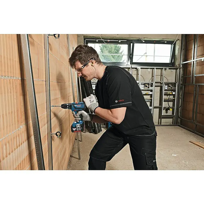Bosch Professional AMPShare 18V Akku-Schlagbohrschrauber GSB 18V-28 - 18 V, 2 Akkus, 2 Ah - 4 Ah, 63 Nm, Inkl. Zubehörkoffer - Ein Handwerker benutzt einen Bosch Akku-Bohrschrauber, um in einer Baustelle eine Metallschiene an einer Ziegelwand zu befestigen.