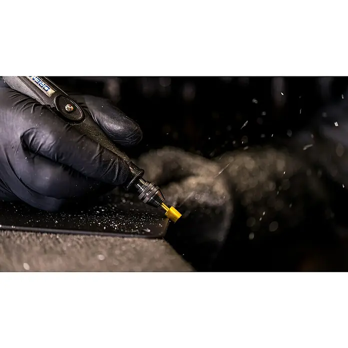Dremel Graviermesser Max 115DM - Arbeitsdurchmesser: 7,9 mm, 2 Stk. - Nahaufnahme eines Dremel-Werkzeugs in Aktion, das feine Späne erzeugt. Handwerker mit Schutzhandschuhen bearbeitet präzise ein Materialstück mit dem Dremel.