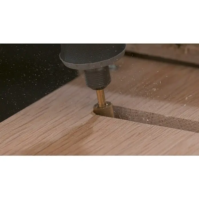 Dremel Graviermesser Max 115DM - Arbeitsdurchmesser: 7,9 mm, 2 Stk. - Ein Werkzeug fräst präzise eine Nut in ein Holzbrett, wobei Späne aufgewirbelt werden. Perfekt für detaillierte Holzarbeiten.