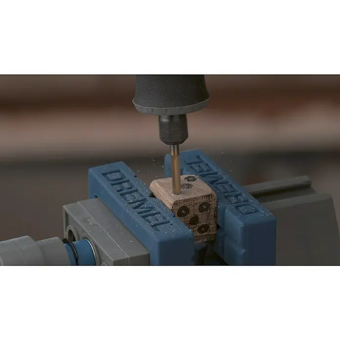 Dremel Fresa de alta velocidad 9903DM - Diámetro de trabajo: 3,2 mm, Redonda - Una herramienta Dremel perfora con precisión agujeros en un dado de madera, sujeto en un tornillo de banco. Ideal para manualidades detalladas y proyectos de bricolaje.