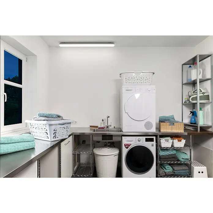 Ledvance LED-Feuchtraumlichtleiste SubmarineLänge: 150 cm, Lichtfarbe: Neutralweiß, 48 W, IP65 - Waschküche mit Waschmaschine und Trockner, Arbeitsfläche und Regalen. Die Waschgeräte sind weiß und modern. Die Regale bieten zusätzlichen Stauraum.