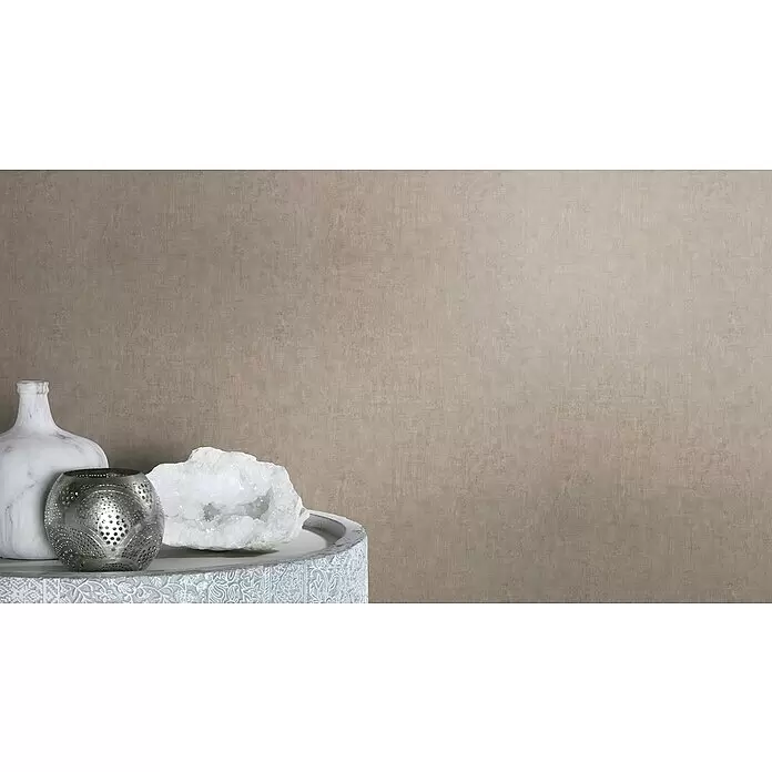Rasch Factory 4 Vliestapete - Braun, Uni, 10,05 x 0,53 m - Dekorative Objekte: eine weiße Marmorvase, ein silberner perforierter Teelichthalter und ein weißer Geodenkristall, auf einem hellgrauen Tisch arrangiert.