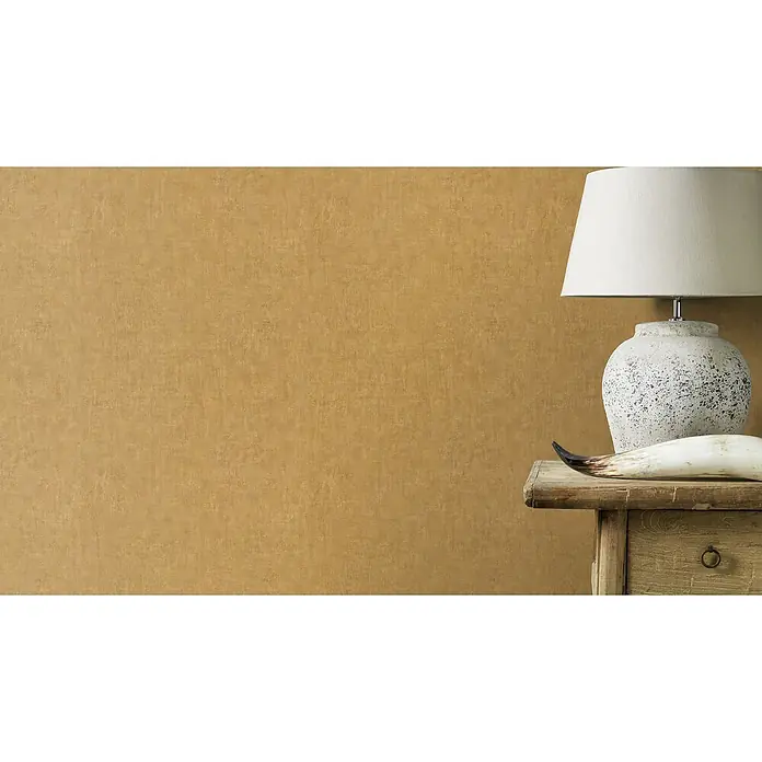 Rasch Factory 4 Vliestapete - Gold, Uni, 10,05 x 0,53 m - Stimmungsvolles Ambiente mit einer eleganten Tischlampe, die auf einem rustikalen Holztisch neben einem dekorativen Horn platziert ist.