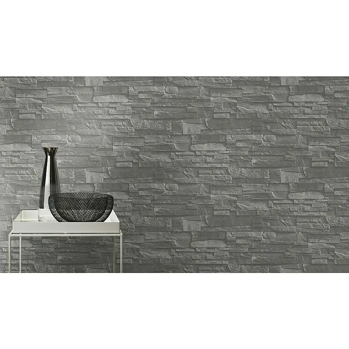 Rasch Vliestapete Steinoptik - Grau/Silber/Schwarz, 3D-Optik, 10,4 x 0,53 m - Nahaufnahme einer stilvollen Dekoration mit Vase und Schale auf einem weißen Tisch vor einer grauen Steinwand. Elegantes Interieur-Detail.