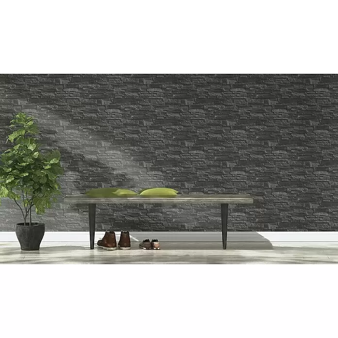 Rasch Vliestapete Steinoptik - Grau, 3D-Optik, 10,4 x 0,53 m - Dunkle graue Bruchsteinwand in einem Raum mit Holzbank und Pflanze, von Sonnenlicht beleuchtet.