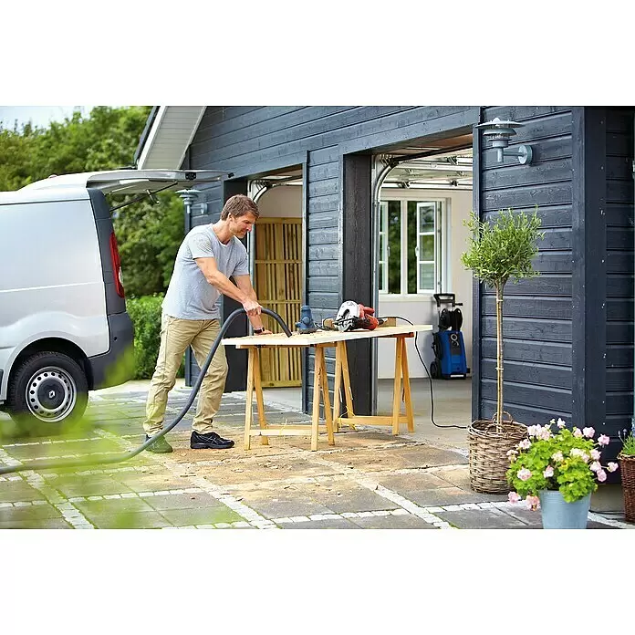 Nilfisk Elektro-Nass- & Trockensauger Multi II 22 - 1.200 W, Behältervolumen: 22 l - Mann reinigt Sägespäne von einer Werkbank mit einem grauen Staubsaugerschlauch.