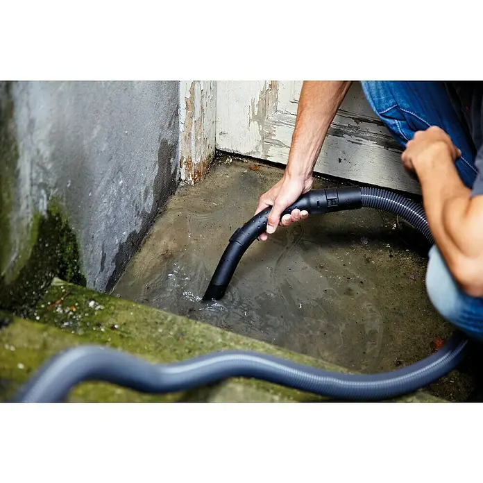 Nilfisk Elektro-Nass- & Trockensauger Multi II 22 - 1.200 W, Behältervolumen: 22 l - Ein Mann saugt mit einem Nass-/Trockensauger Wasser aus einem überfluteten Bereich in einem Haus, um das stehende Wasser zu beseitigen.