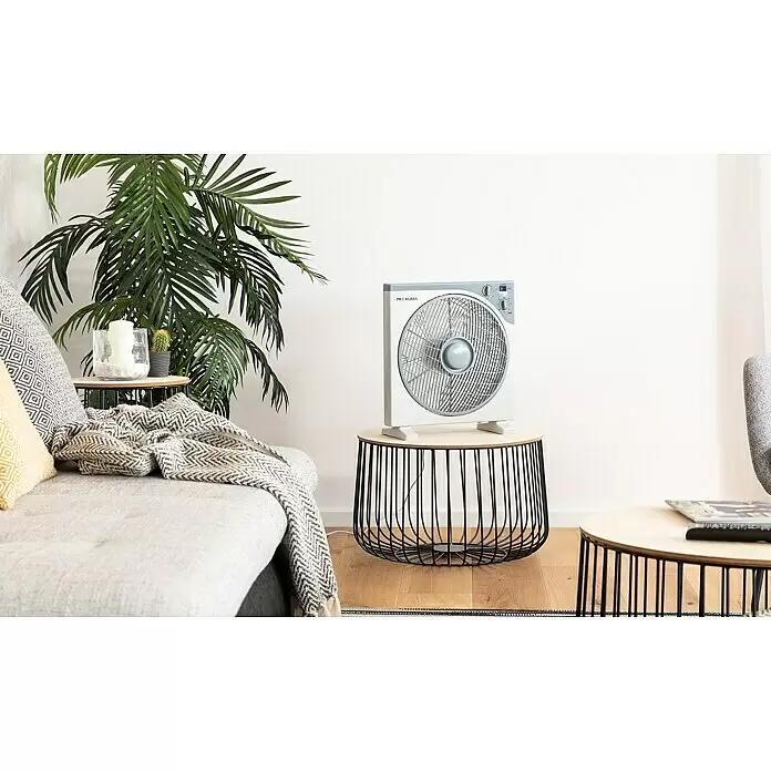 PR Klima Ventilador de suelo Box Fan - 50 W, Blanco/gris, 30 cm - Ventilador de caja blanco con rejilla gris, colocado sobre una mesa auxiliar de madera y metal negro en una sala de estar moderna.
