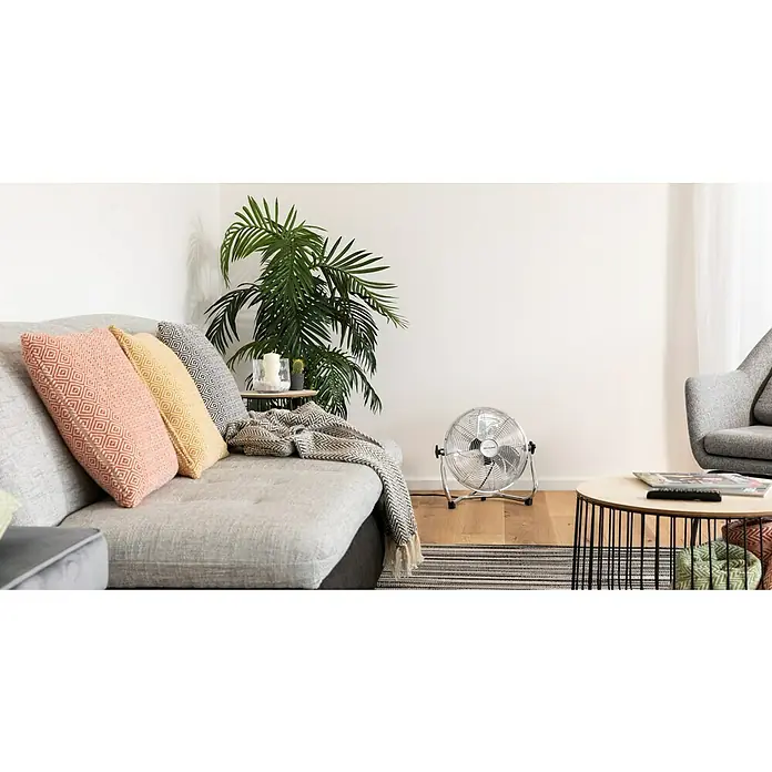 PR Klima Ventilador de suelo Speed - 40 W, Plateado, 30 cm - La imagen muestra un ventilador de pedestal Miele en una sala de estar moderna con sofá, planta y suelo de madera.
