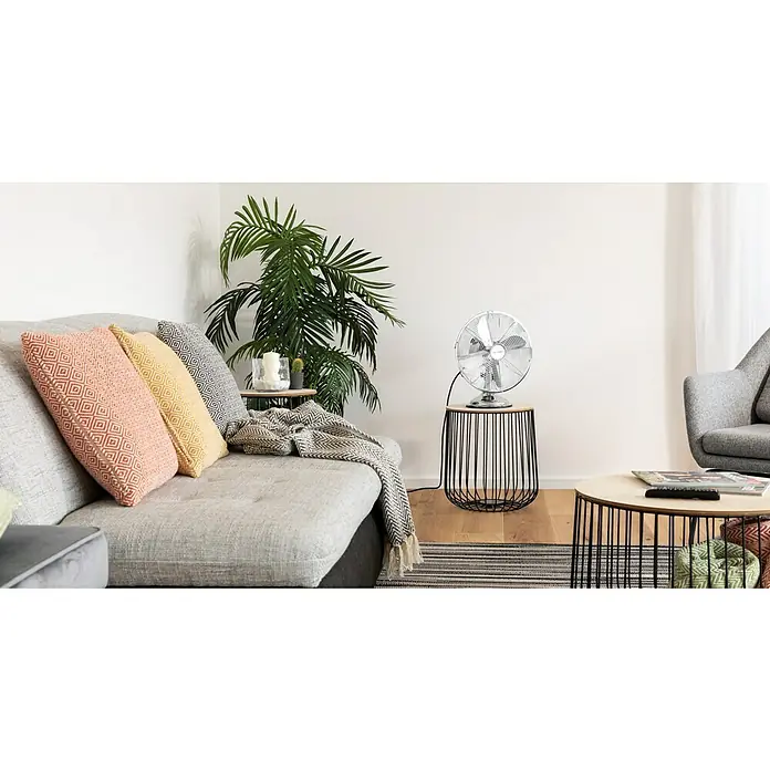 Voltomat Tischventilator - Silber, 30 cm - Das Wohnzimmer verfügt über ein graues Sofa mit bunten Kissen, einen Beistelltisch mit Ventilator und eine Zimmerpflanze, die eine gemütliche Atmosphäre schaffen.