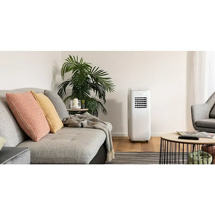 PR Klima Aire acondicionado portátil Purity 9000 - 2.600 W, Tamaño de la estancia: 26 m², Blanco/Plateado - Una sala de estar moderna con un aire acondicionado portátil en blanco, junto a un sofá adornado con cojines y una mesa auxiliar con plantas.