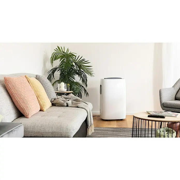 TCL Mobiles Klimagerät TAC-07CPA/HA - 2,2 kW, Raumgröße: 22 m², Weiß/Silber - Ein moderner Wohnraum mit einem tragbaren Luftentfeuchter, der für saubere Luft und Komfort sorgt, neben einer Couch mit dekorativen Kissen.