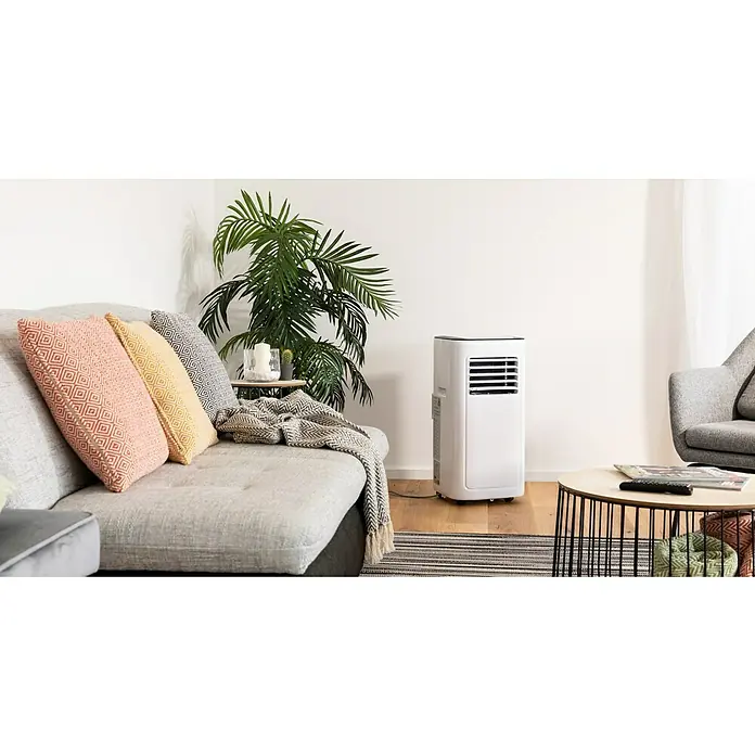 Voltomat Aire acondicionado portátil Boreas - 2.000 W, Tamaño de la estancia: 20 m², Blanco/Negro - Un aire acondicionado portátil está al lado de un sofá con cojines y una planta de interior, perfecto para la estación cálida.