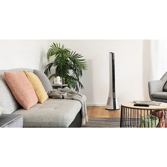 PR Klima Ventilador de torre Design - Blanco/Negro, 110 cm, 40 W - Un moderno ventilador de torre en una elegante sala de estar. El delgado ventilador con carcasa blanca se encuentra junto a una planta de interior verde.