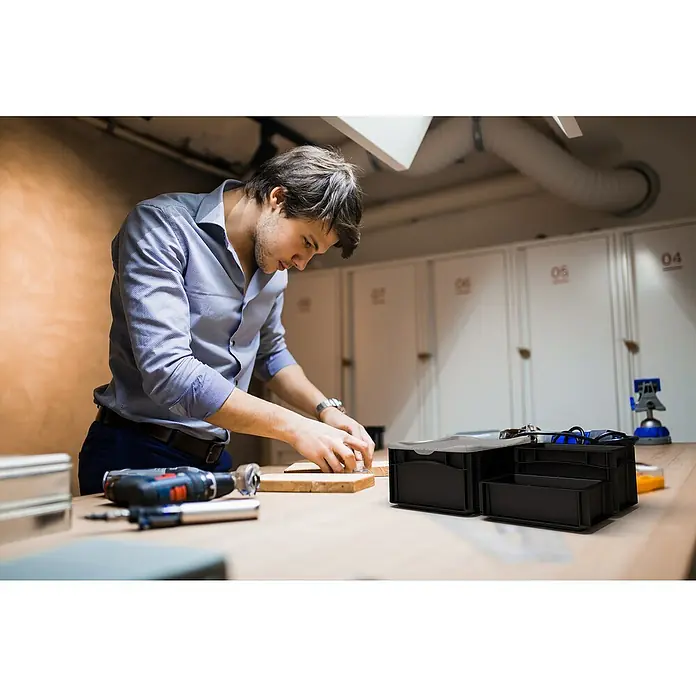 Surplus Systems Eurobox - L x B x H: 40 x 30 x 12 cm, Kunststoff, Schwarz - Ein Mann arbeitet mit einem Werkzeugkasten, einem Akkuschrauber und Holz auf einer Werkbank, umgeben von Werkzeugen und Geräten.