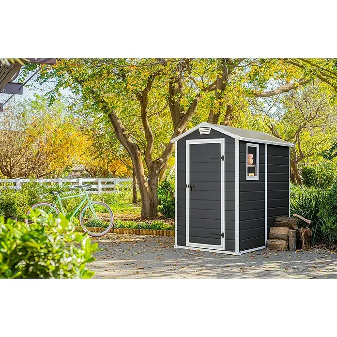 Keter Gerätehaus Manor 4x6 - Außenmaß inkl. Dachüberstand (B x T): 130 x 192 cm, Kunststoff, Anthrazit/Weiß - Gartenszene mit einem anthrazitfarbenen Gerätehaus mit weißem Rahmen, das praktischen Stauraum im Freien bietet.\n