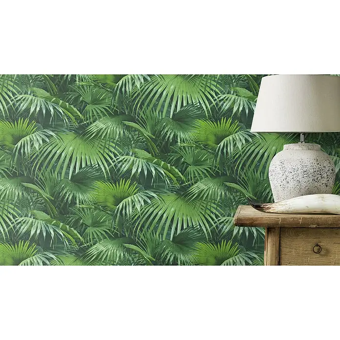 Rasch Crispy Paper Vliestapete Dschungel - Grün, Floral, 10,05 x 0,53 m - Nahaufnahme einer Tischlampe mit einem weißen Lampenschirm und einem rustikalen Sockel, platziert auf einem hölzernen Nachttisch vor einer Dschungeltapete.