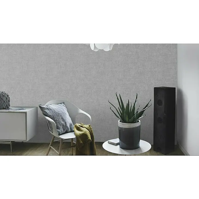 Rasch Vliestapete - Dunkelgrau, Uni, 10,05 x 0,53 m, Schimmernd - Wohnzimmer mit grauer Tapete an der Wand, Akzentstuhl mit Kissen und Decke, einem Lautsprecher und einer Zimmerpflanze im Topf.