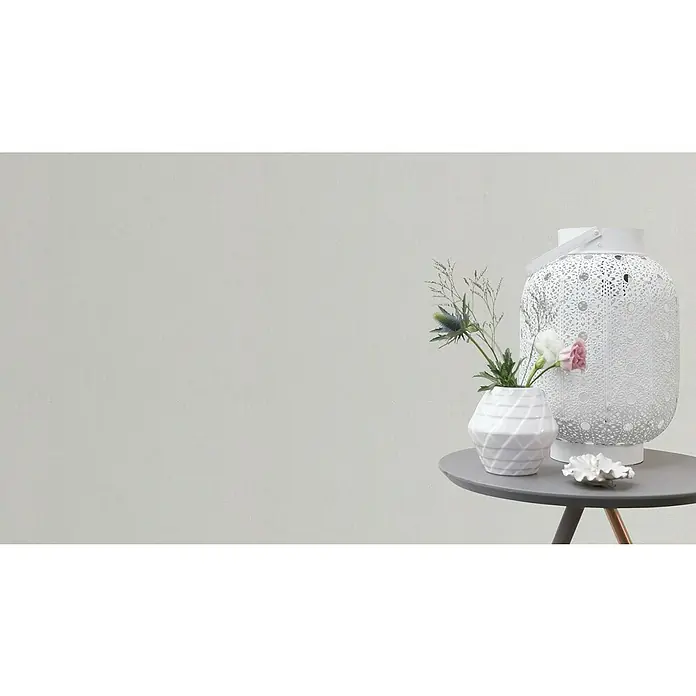 Rasch Vliestapete - Beige/Creme, Uni, 10,05 x 0,53 m, Schimmernd - Dekorative Tischszene mit einer weißen Laterne, einer Vase mit Blumen und einer Muschel auf einem grauen Tisch vor einem neutralen Hintergrund.