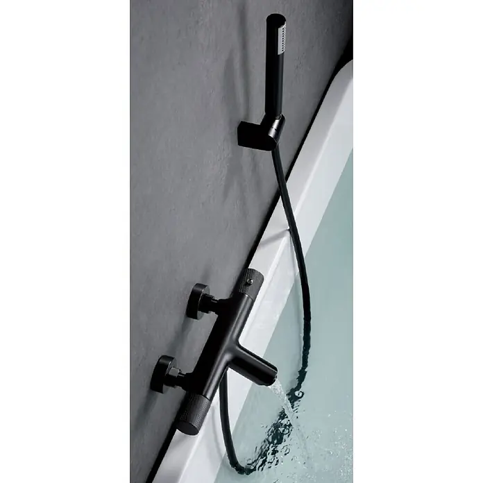 Imex Line Grifo termostático de bañera - Black gun metal - Grifo de bañera negro con teleducha montado en una pared gris que vierte agua en una bañera blanca.