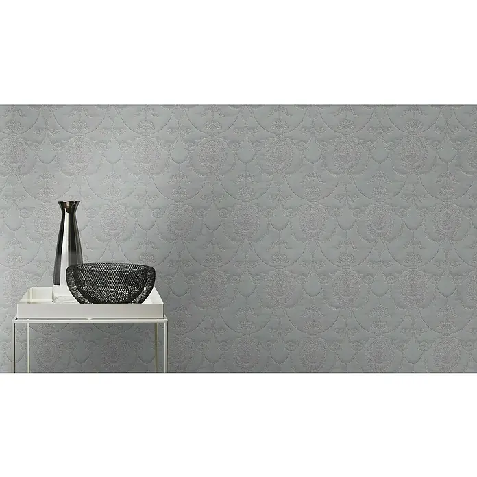 Rasch Trianon Vliestapete II - Dunkelgrau, Ornament, 10,05 x 0,53 m - Elegante Tischdekoration mit einer schlanken Vase und einer dekorativen Schale auf einem stilvollen Beistelltisch vor gemusterter Wand.