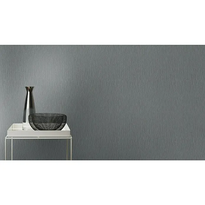 Rasch Berlin Vliestapete - Dunkelgrau, Uni, 10,05 x 0,53 m - Ein elegantes Stillleben mit einer silbernen Vase und einer dekorativen Schale auf einem weißen Beistelltisch vor einer grauen Wand.