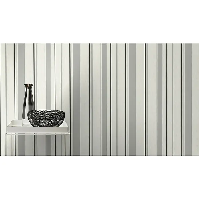 Rasch Rock'n Rolle Vliestapete Stripes - Weiß/Grau/Schwarz, Streifen, 10,05 x 0,53 m - Stillleben mit schlanker Vase und dekorativer Schale auf einem Beistelltisch, vor einer gestreiften Wand.
