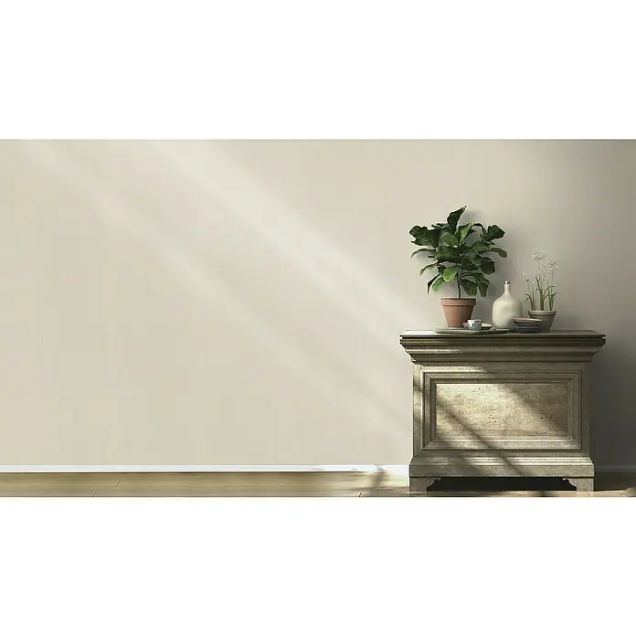 Rasch BARBARA Home Collection II Vliestapete - Dunkelbeige, Uni, 10,05 x 0,53 m - Eine elegante Kommode mit Pflanzen und Dekorationen, beleuchtet von einem sanften Lichtstrahl, verleiht dem Raum eine warme Atmosphäre.