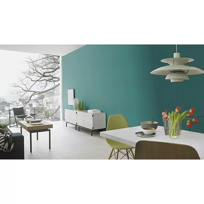 Rasch BARBARA Home Collection II Vliestapete - Türkis, Uni, 10,05 x 0,53 m - Ein moderner Wohnraum mit einer kräftigen, türkisfarbenen Strukturwand, die einen lebendigen Hintergrund für minimalistische Möbel bildet.