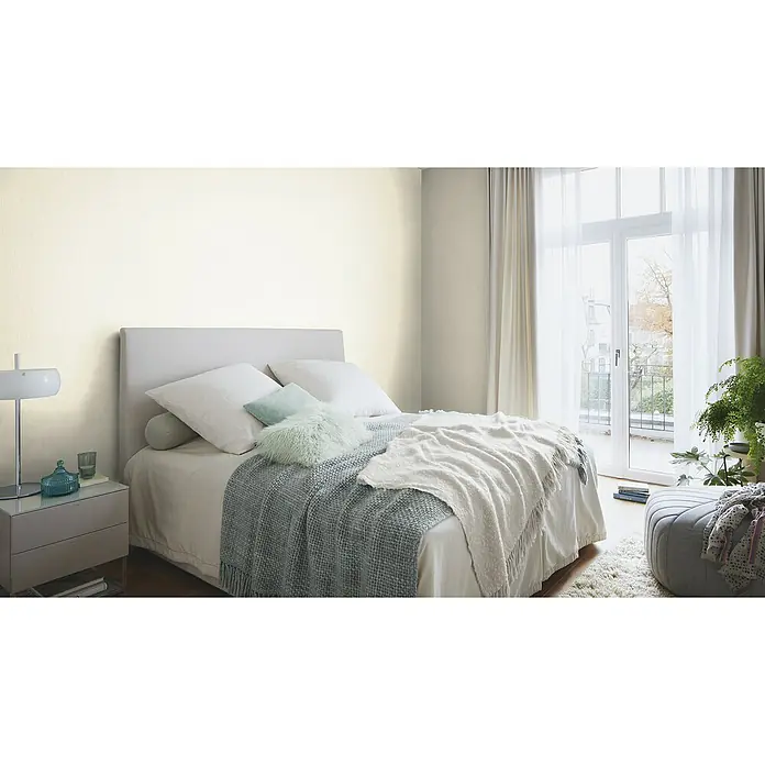 Rasch Selection Vliestapete I - Creme, Uni, 10,05 x 0,53 m - Helles Schlafzimmer mit einem Bett, das mit Kissen und Decken dekoriert ist, und einem Nachttisch mit Lampe.