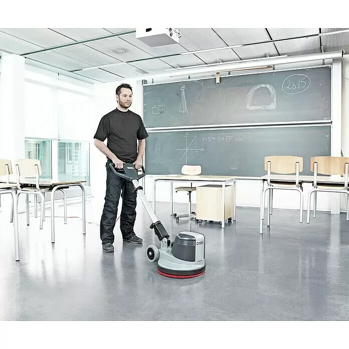 Nilfisk Poliermaschine FM400 D - 1.500 W - Ein Mann bedient eine grau-schwarze Nilfisk Bodenreinigungsmaschine mit rotem Pad in einem Klassenzimmer.