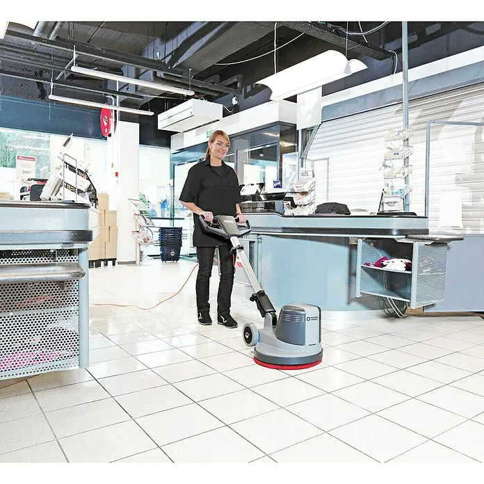 Nilfisk Poliermaschine FM400 D - 1.500 W - Frau reinigt mit einem Nilfisk Bodenreiniger einen weißen Fliesenboden in einem Geschäft.