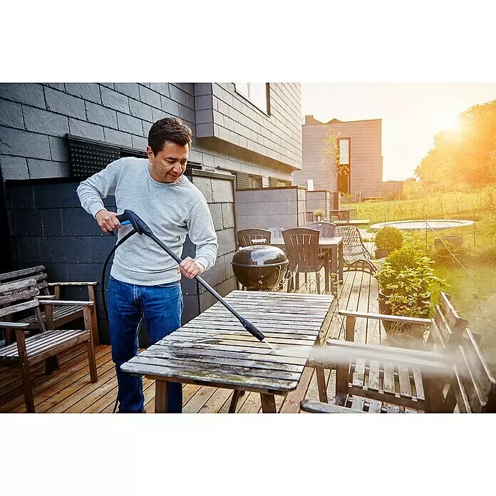 Nilfisk Hochdruckreiniger C 135.7-6 Garden X-tra - 1.500 W, Max. Druck: 135 bar, Fördermenge: 460 l/h - Mann reinigt mit einem Hochdruckreiniger einen schmutzigen Holztisch auf einer Terrasse.