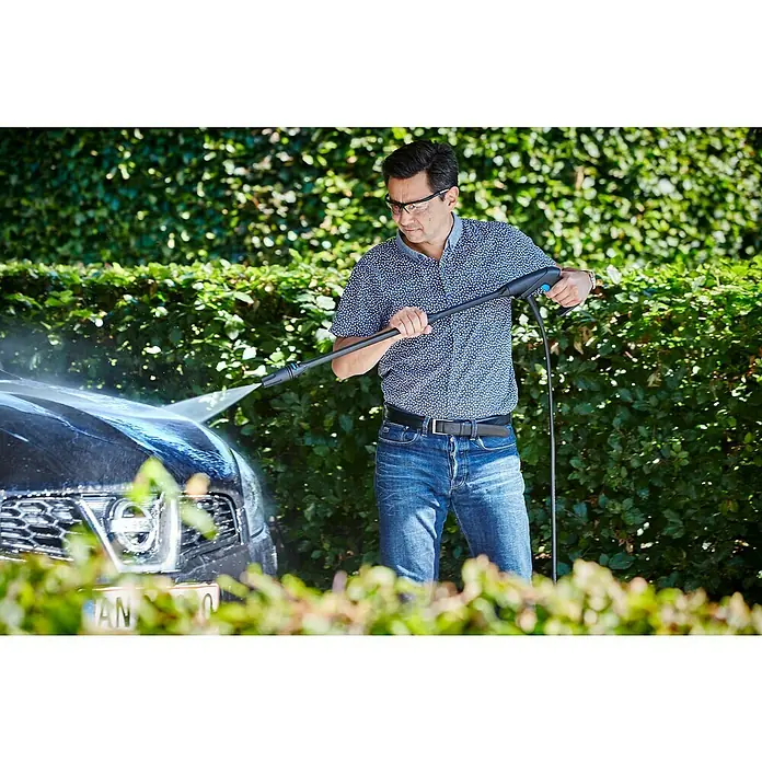 Nilfisk Hochdruckreiniger C 135.7-6 Garden X-tra - 1.500 W, Max. Druck: 135 bar, Fördermenge: 460 l/h - Mann reinigt ein schwarzes Auto mit einem Hochdruckreiniger vor einer grünen Hecke. Das Gerät entfernt Schmutz und sorgt für Glanz.