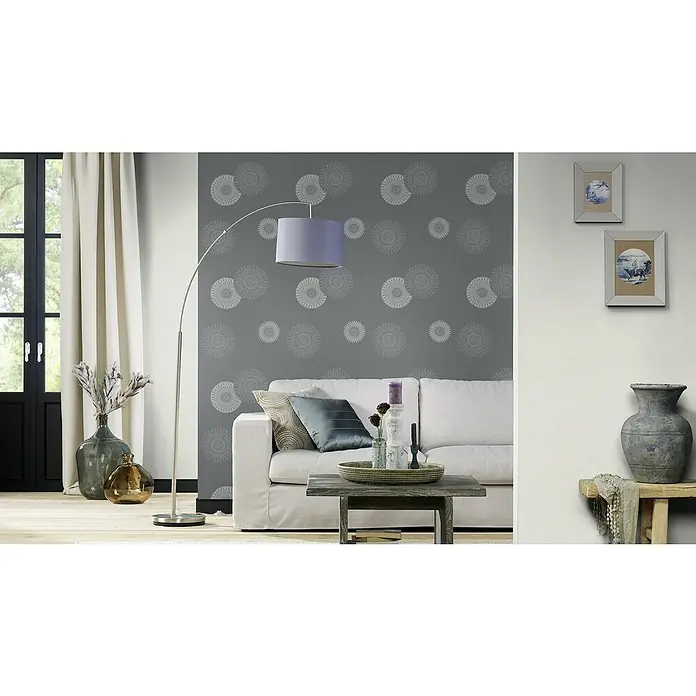 Rasch Tapetenwechsel Vliestapete - Dunkelgrau, Grafisch, 10,05 x 0,53 m - Wohnzimmer mit grau gemusterter Tapete, Stehlampe und weißem Sofa. Dekorative Accessoires wie Vasen und Bilderrahmen ergänzen das Ambiente.