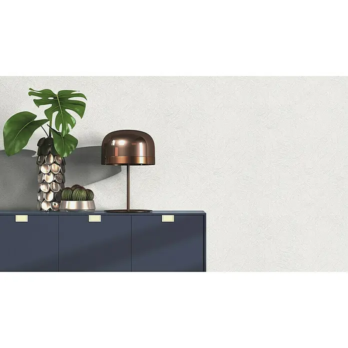 Rasch Vliestapete - Beige/Creme, Uni, 10,05 x 0,53 m, Spachtelstruktur - Nahaufnahme eines blauen Sideboards mit Topfpflanzen und einer stilvollen bronzefarbenen Lampe vor einer strukturierten weißen Wand.