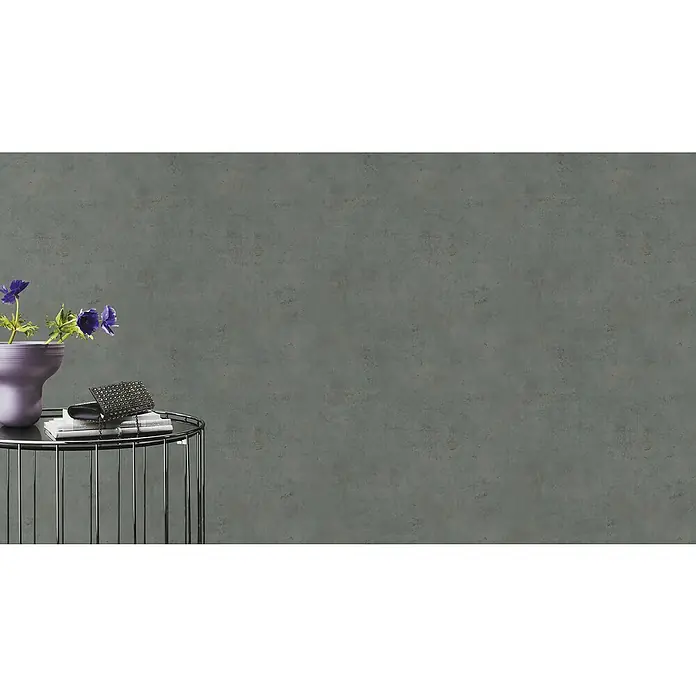 Rasch Vliestapete Beton - Dunkelgrau, Betonoptik, 10,05 x 0,53 m - Nahaufnahme eines stilvollen Tisches mit einer Vase mit Blumen, Büchern und einer eleganten Clutch vor einem neutralen Hintergrund.