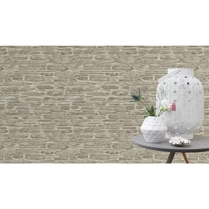 Rasch Tapetenwechsel Vliestapete - Beige, 10,05 x 0,53 m - Ein dekorativer Tisch mit einer weißen Laterne, einer Vase mit Blumen und einer kleinen Dekoschale vor einer rustikalen Steinwand.