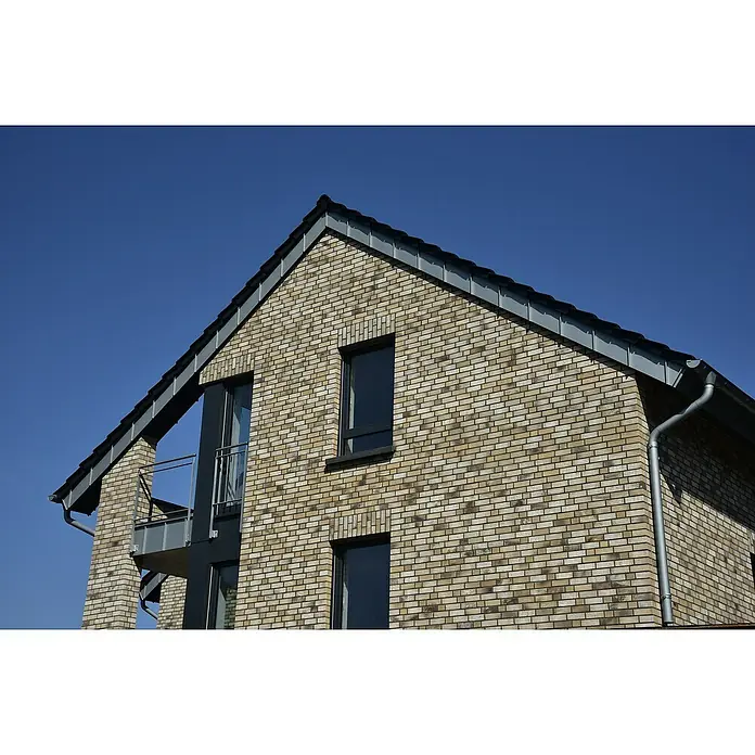 Celina Klinker Verblendstein-Ecke Handstrich Valencia - 21,5 x 6,5 x 10,25 cm, Beige, Steinoptik - Nahaufnahme eines modernen Hauses mit Ziegelfassade, markanten Fenstern und grauen Dachelementen vor einem strahlend blauen Himmel.