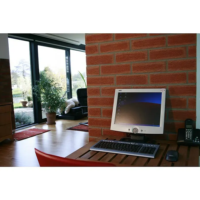 Celina Klinker Verblendstein-Ecke Handform Rotsand - 11,5 cm x 5,2 cm x 7 mm, Rot, Steinoptik - Ein AOC Monitor mit Tastatur und Maus auf einem Holztisch vor einer Ziegelwand. Daneben steht ein Telefon.