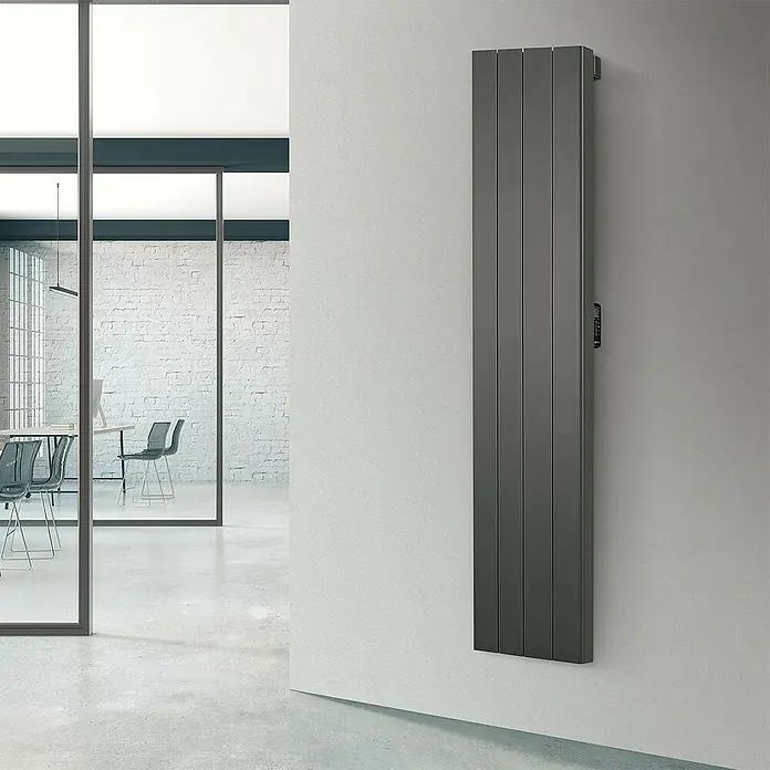 Rointe Radiador eléctrico digital Palaos - 2.000 W, Negro, 110 x 476 x 1.800 mm - Un moderno panel de calefacción gris está montado en una pared blanca en una habitación luminosa. El panel es delgado y alto, con nervios verticales.