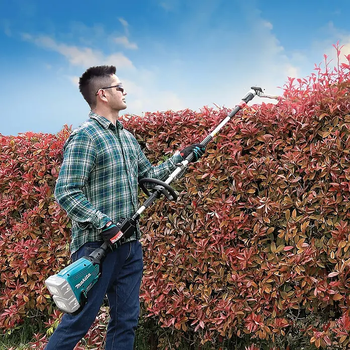 Makita LXT 18V Akku-Multifunktionswerkzeug DUX60Z - 36 V, Ohne Akku - Ein Mann bedient eine Makita Akku-Heckenschere mit Teleskopstiel, um eine Hecke zu schneiden. Ideal für Gartenarbeiten.