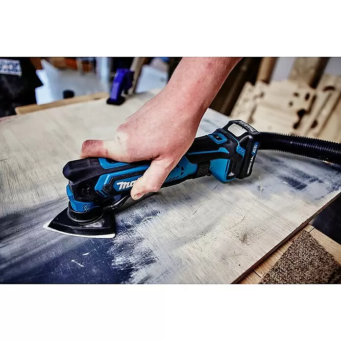 Makita CXT 12V max. Akku-Multifunktionswerkzeug TM30DZ - 12 V, Ohne Akku - Hand hält schwarzes und türkises Makita Multitool mit Schleifaufsatz, schleift Holz, Staubabsaugschlauch angeschlossen.